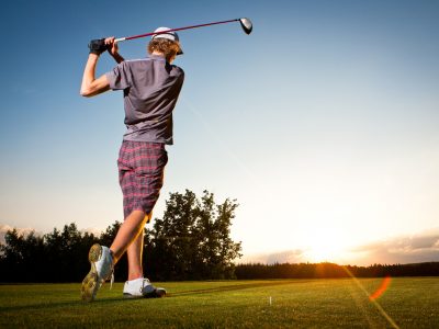 Male golf player teeing off golf ball from tee box to beautiful sunset