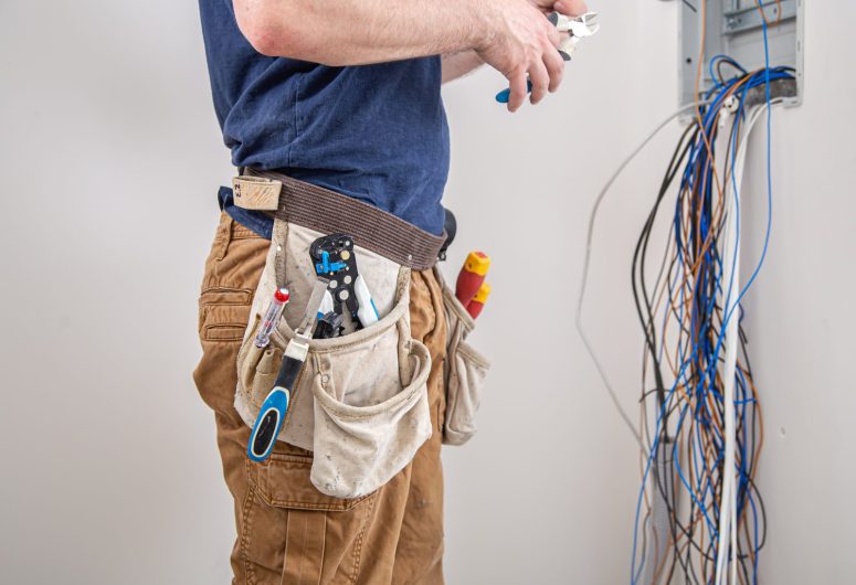 Electrician builder examines the cable connection in the electrical line in switchboard indoor.